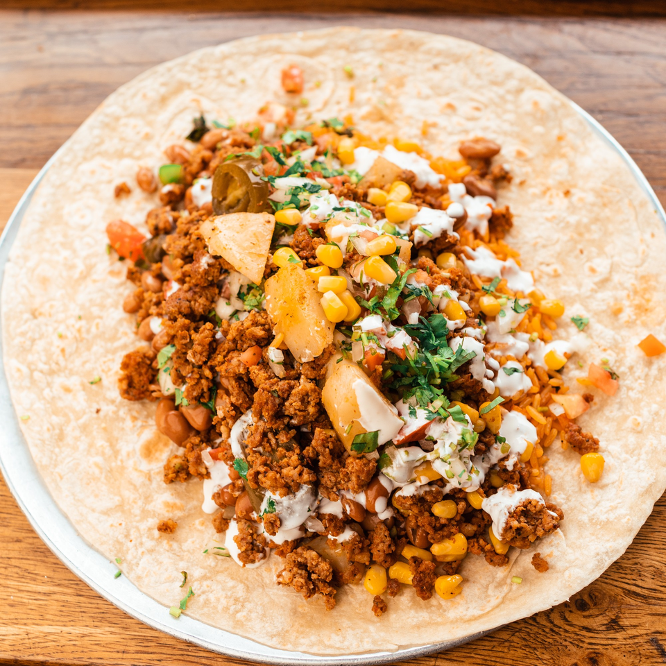 Unrolled burrito with seasoned ground meat, corn, potatoes, jalapeños, and white sauce on a tortilla.