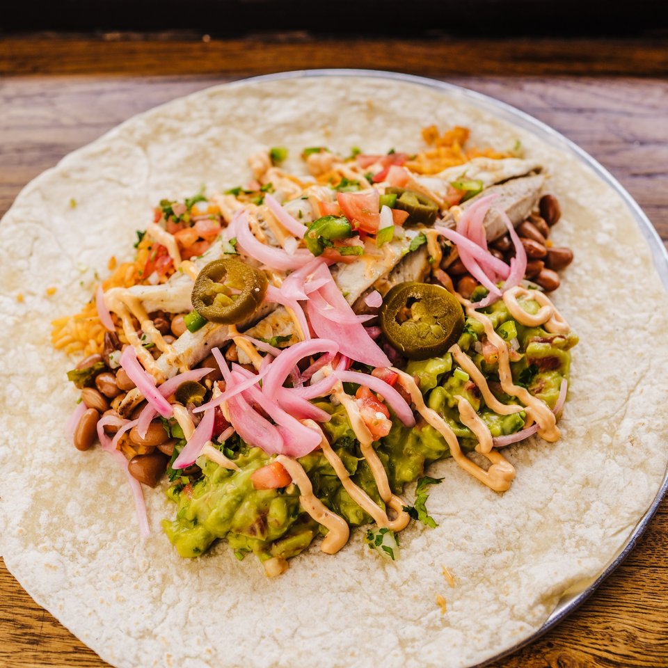 An open Burrito Republic burrito with chicken, beans, rice, guacamole, pickled onions, and jalapeños.