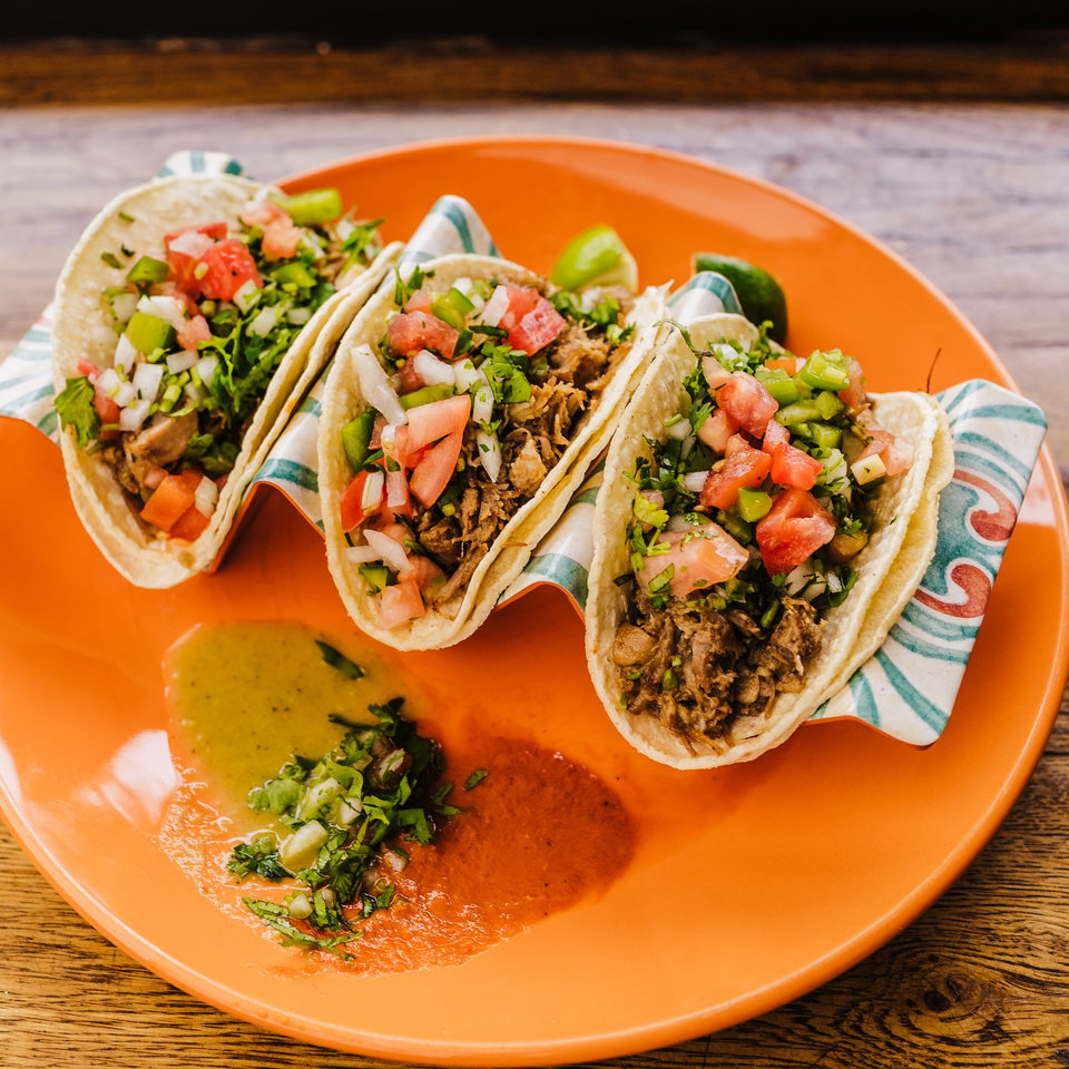 Three Burrito Republic tacos with meat, pico de gallo, and cilantro on an orange plate.